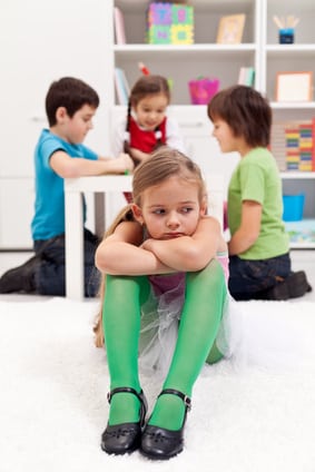 Sad little girl sitting excluded by the other kids